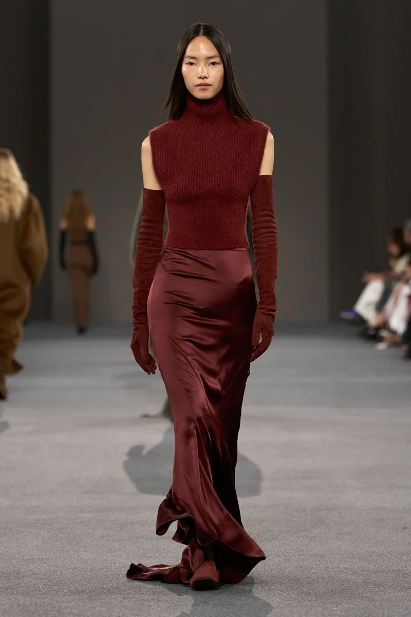 Модель Max Mara в бордовом трикотажном топе с высоким горлом и атласной юбке в пол
