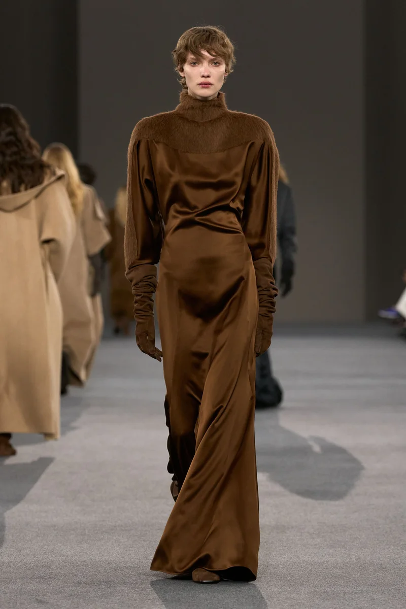 Модель Max Mara в шоколадном атласном платье с высоким горлом и перчатках в тон