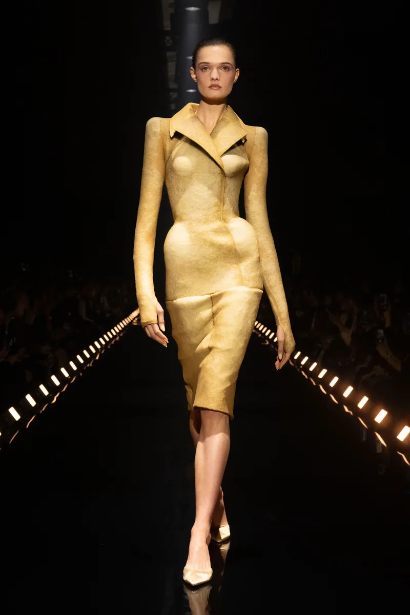 Модель Schiaparelli в золотом облегающем платье с широкими лацканами