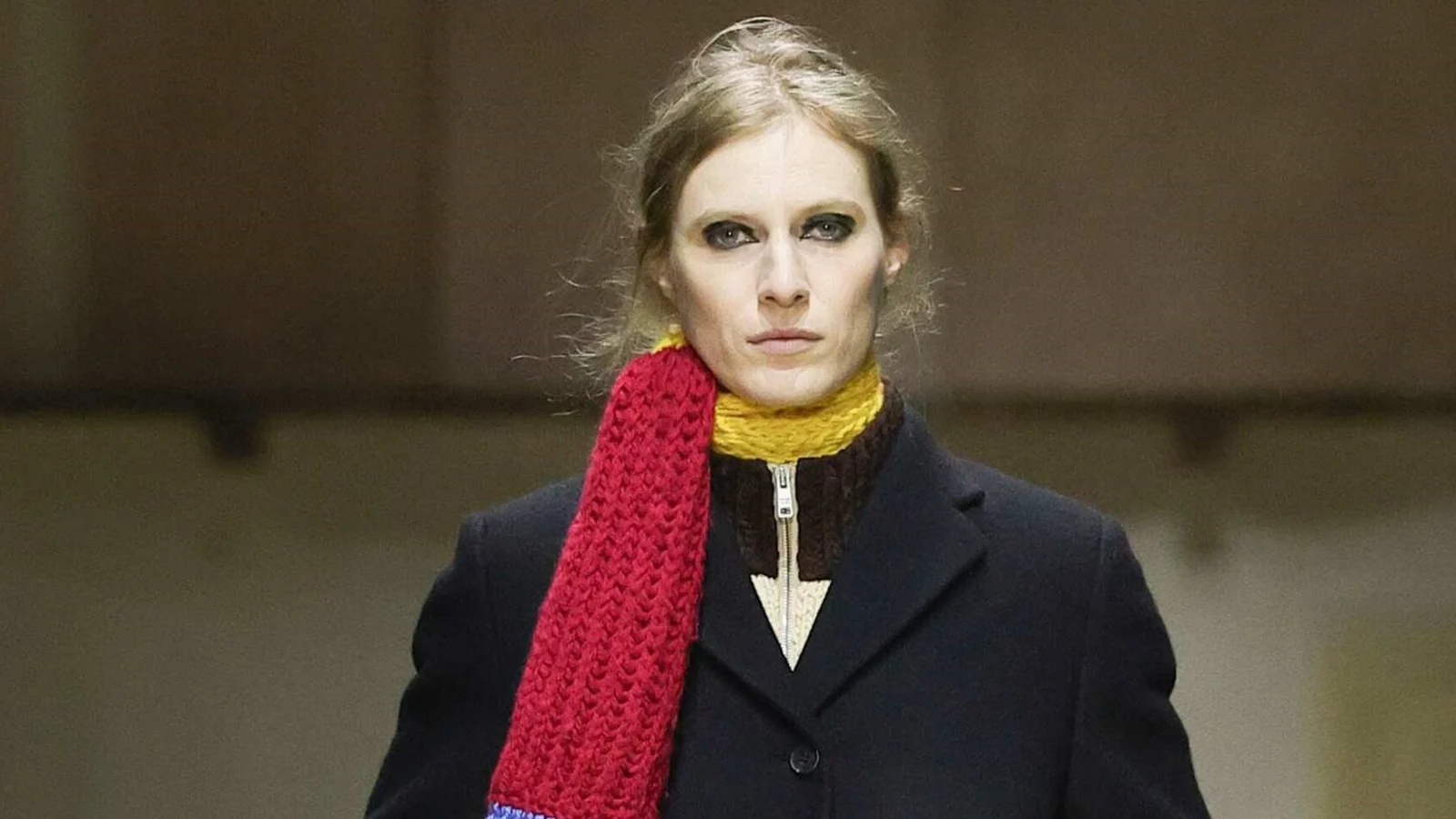 Красный вязаный шарф с бахромой поверх черного пальто на показе Prada осень-зима 2026-2027