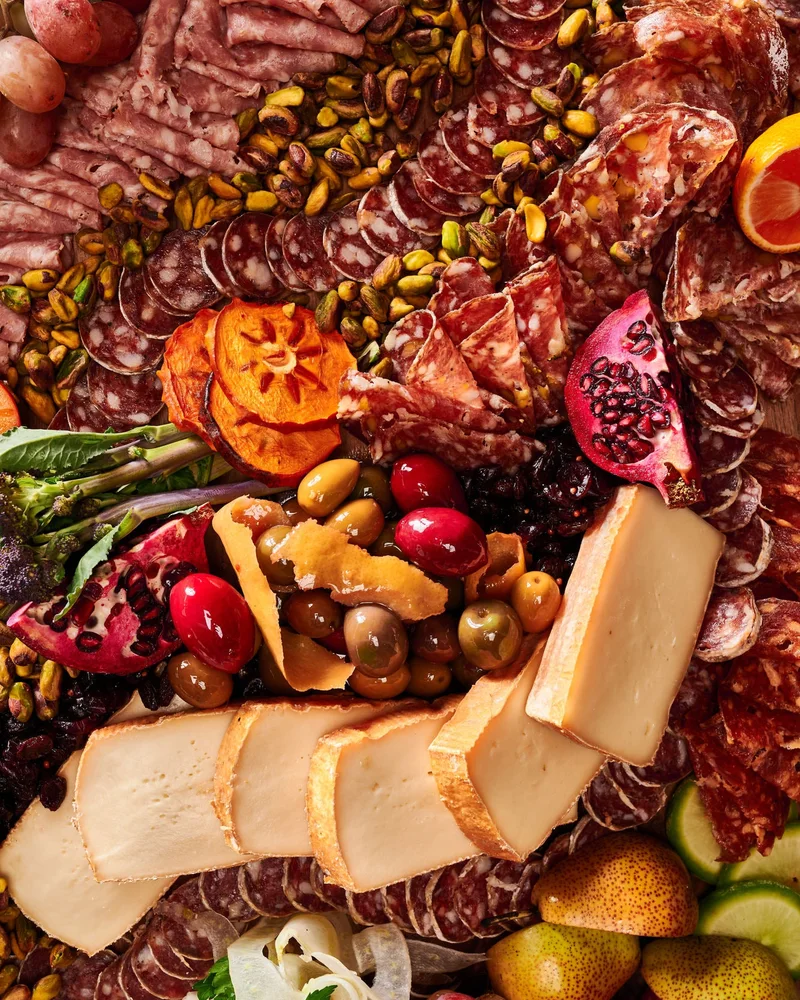 Крупный план мясной доски: ряды салями, пластины сыра, хурма, гранат и груши