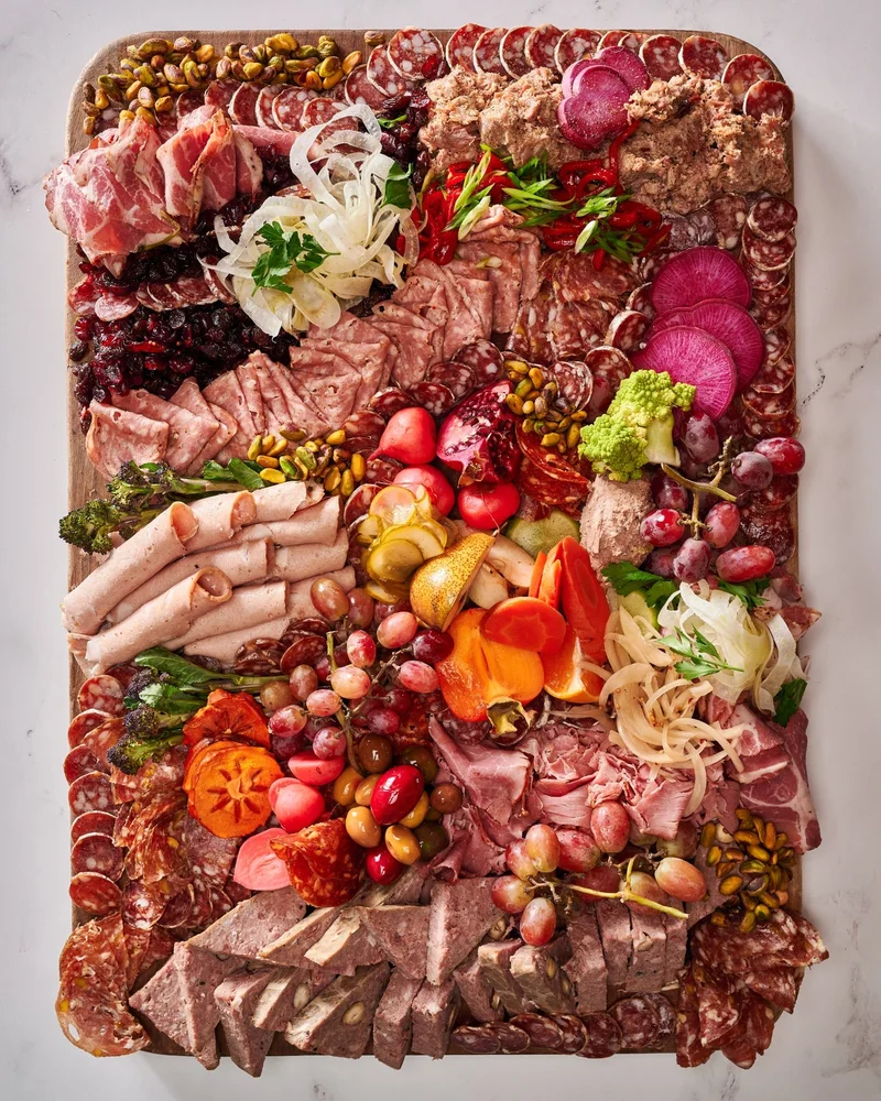 Прямоугольная мясная доска с ветчиной, салями, паштетом, ягодами и овощами, вид сверху