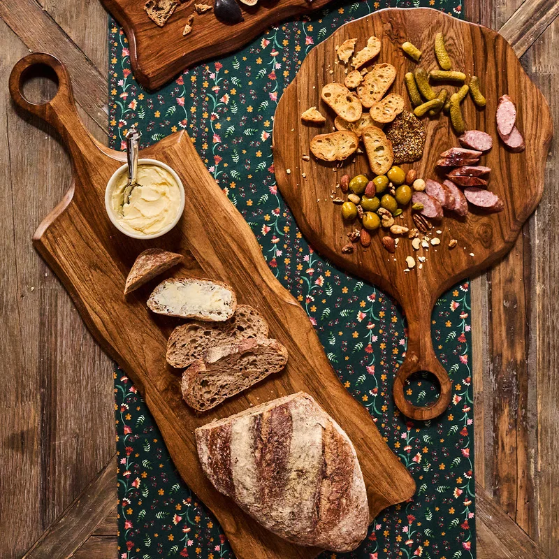 Длинная доска с нарезанным хлебом и соусом рядом с сырной доской